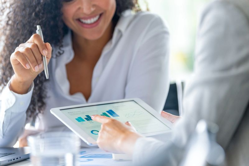 Close up of Two business women meeting and looking at financial data, charts and graphs on a digital tablet. One woman is happy and smiling