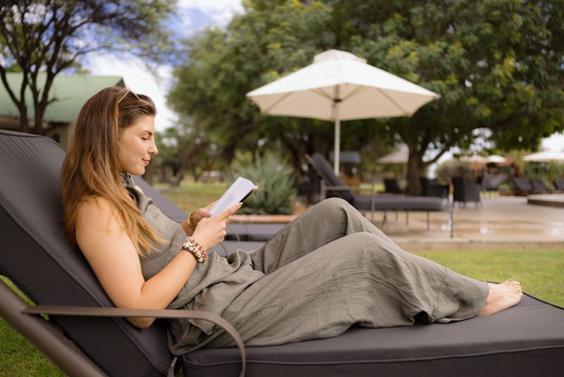 Young woman enjoying a relaxing day reading a book while lounging on a deck chair by the pool at a beautiful resort