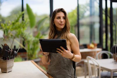 A woman in an apron holding a tablet in a bright café.