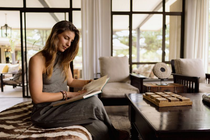 Young woman enjoying a book in a stylish living room, bathed in natural light from expansive windows