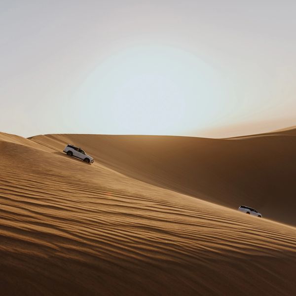 Two SUVs driving on vast sand dunes under a clear sky.