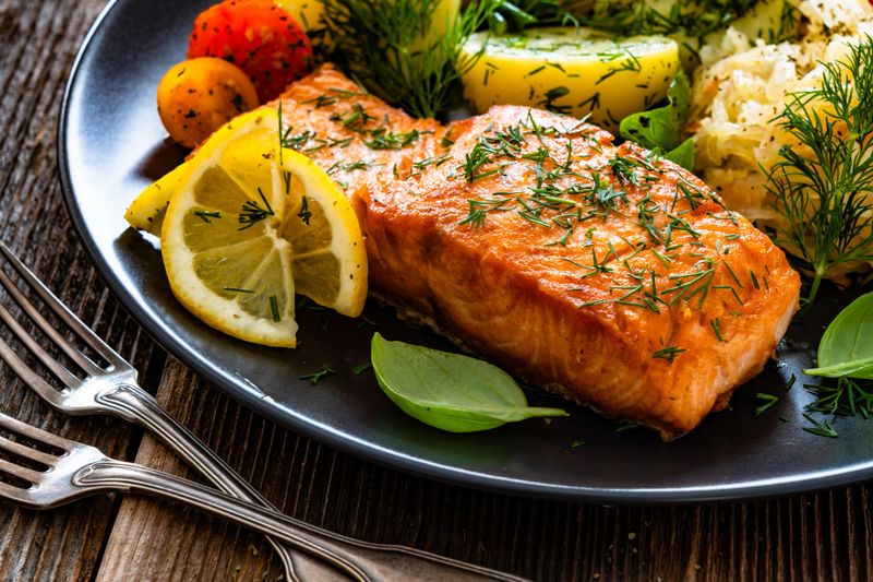 Fried salmon steak with boiled potatoes and sauerkraut served on white plate on wooden background