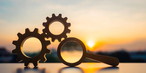 Wooden gears and magnifying glass silhouetted against a sunset.