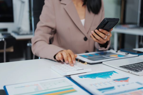 Businessperson using calculator and phone with financial charts.