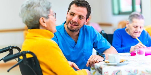 A nurse attentively talks with an elderly woman in a wheelchair at a care facility.