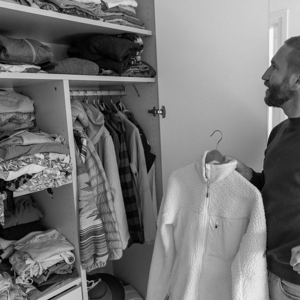 Man holding a white fleece jacket while looking at a wardrobe.