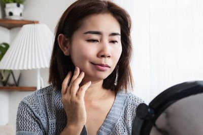 photo of woman with facial paralysis on one side of her face, holding her hand up to her face to tou