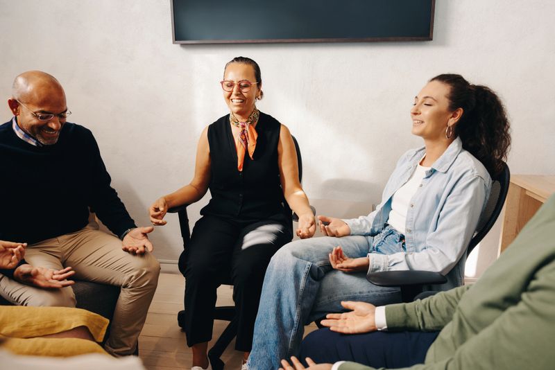 Colleagues sitting in a circle meditating together during a guided exercise, promoting teamwork and wellbeing.