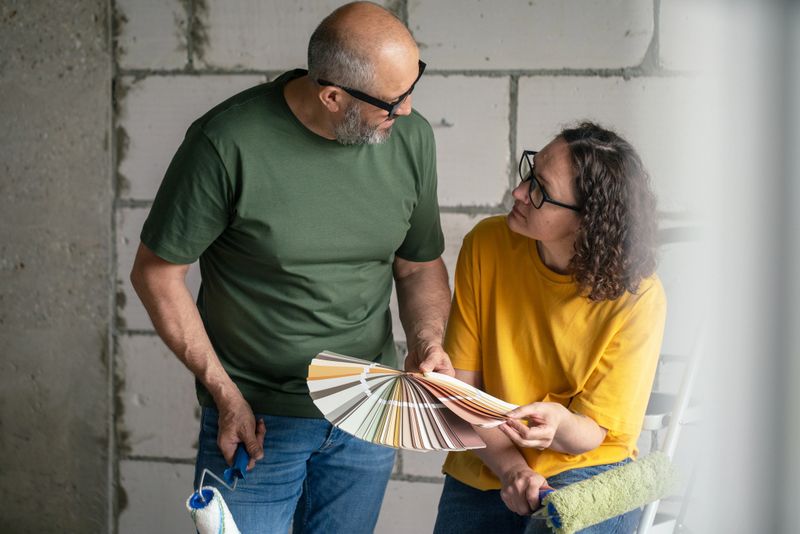 A couple exploring color samples while renovating their home, emphasizing decision-making, teamwork, and creativity in home improvement efforts. Paint rollers and color sample cards in their hands.