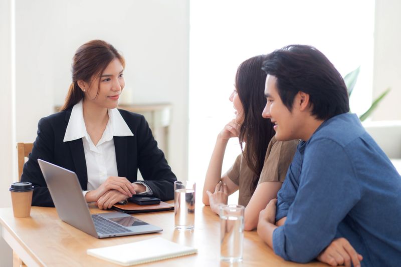 Happy asian couple discussion with real estate agent or insurance agent for investment in home office, mortgage loan or property purchase home, sale explaining insurance plan with couple.