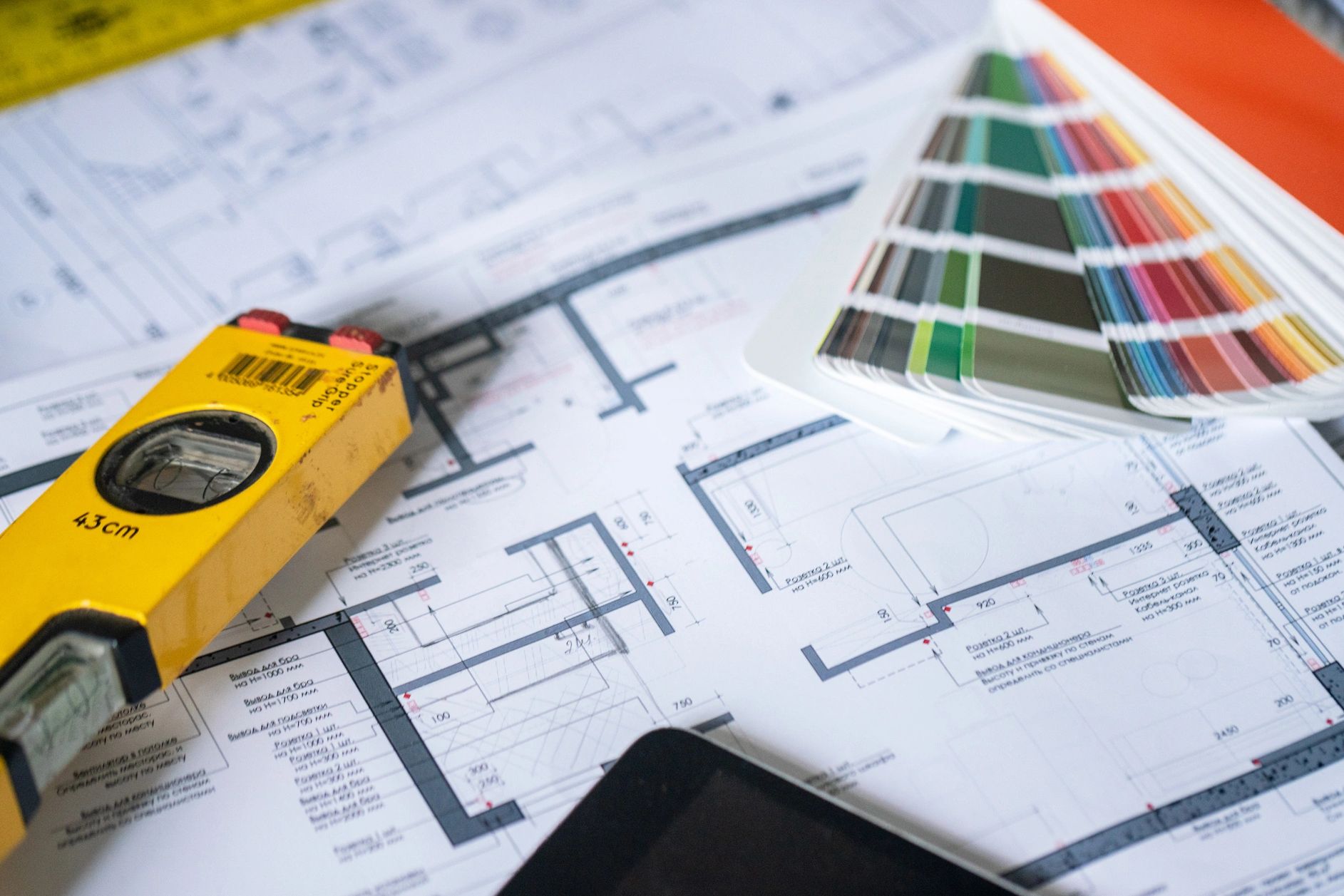 Architectural blueprints with a yellow spirit level and color swatches on a desk.