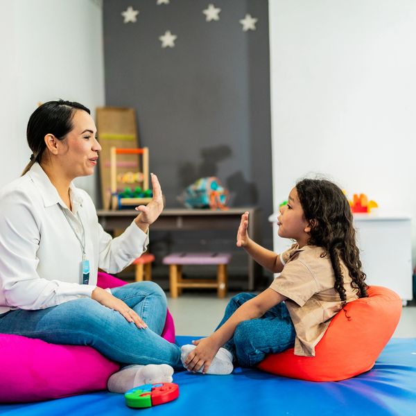 Therapist and child communicating using sign language in a colorful room.