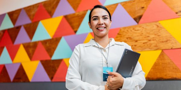 Smiling woman holding a laptop in front of a colorful geometric wall.