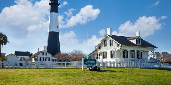 Historic Tybee Island Lighthouse with white picket fence and blue sky.