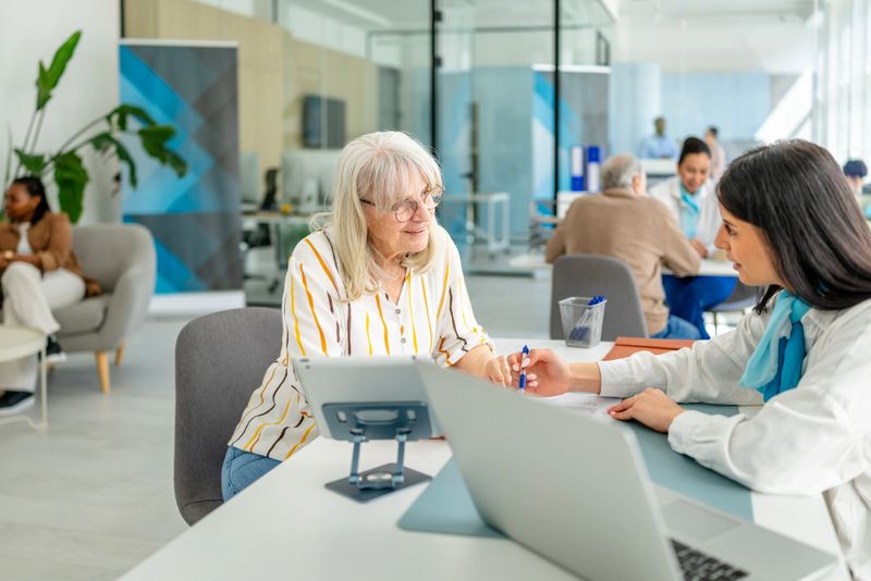 In a contemporary bank office, a financial advisor engages in a detailed discussion with a senior client about banking options. The atmosphere is professional, with diverse clients present.