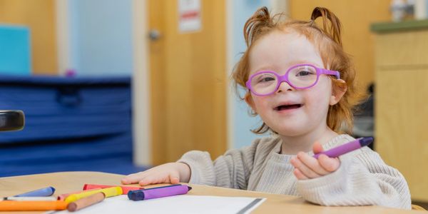 Smiling girl with glasses holding a purple marker.