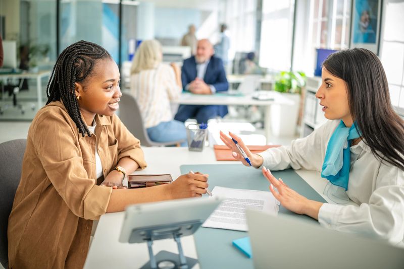 In a contemporary bank office, a female financial advisor interacts with a young client discussing financial services.