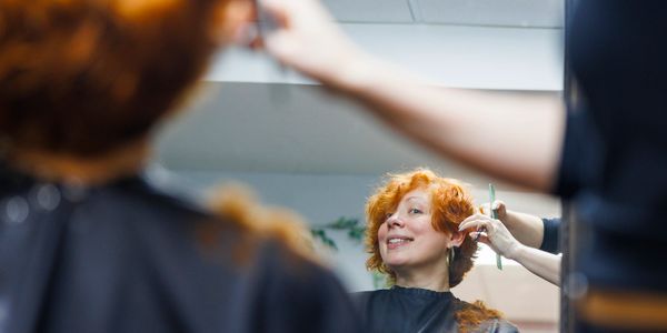 Woman with red hair smiling during a haircut in a salon.
