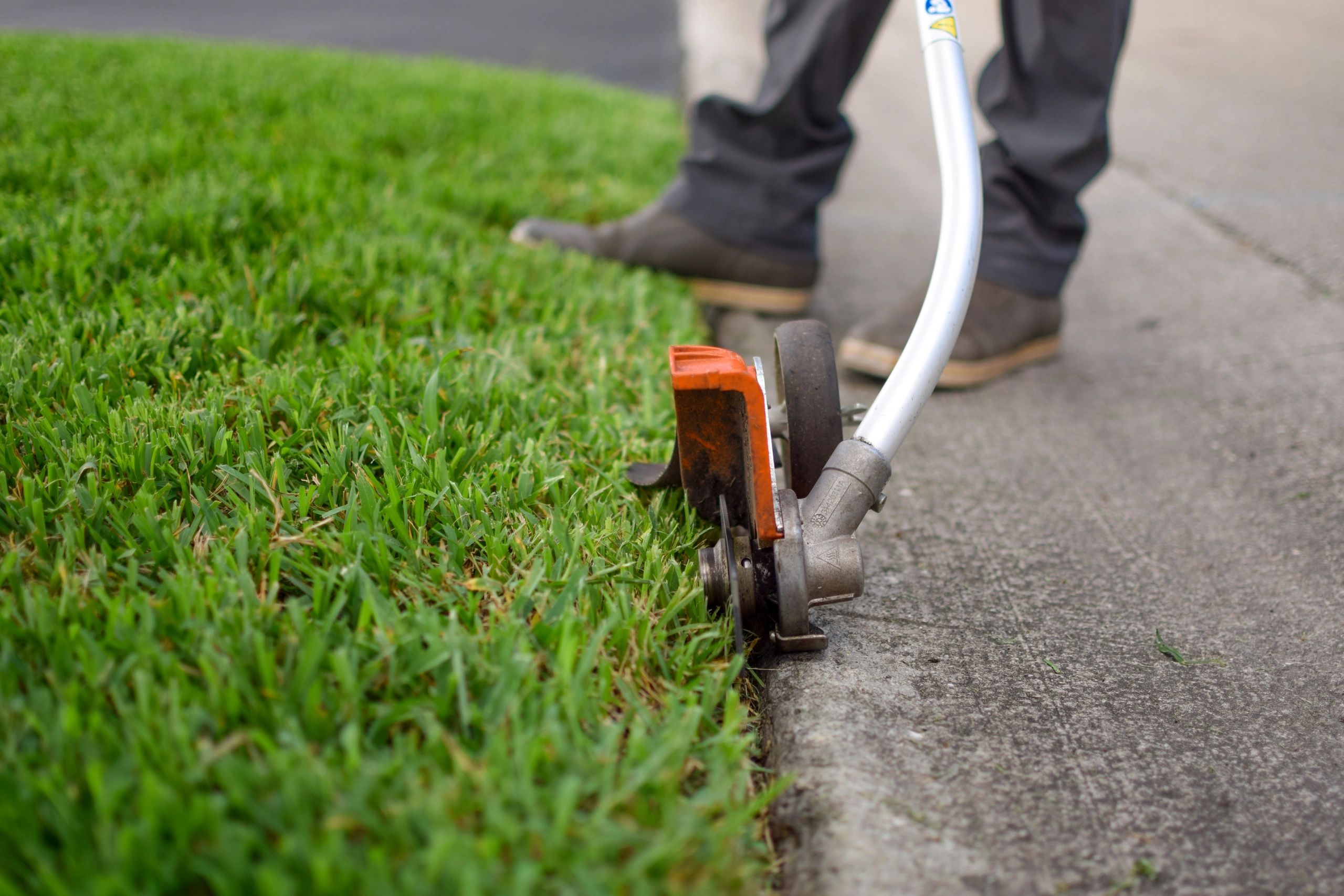 Person trimming grass edges with a string trimmer along a sidewalk.
