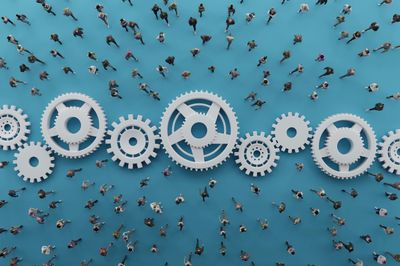 People walking around large interconnected gears on a blue surface.