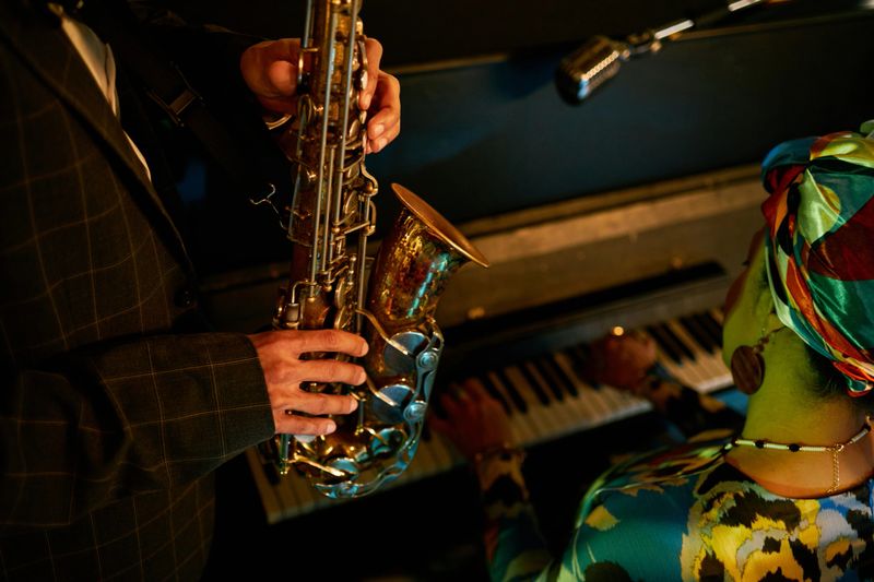 Cropped shot of multiethnic musicians duet improvising on saxophone and piano during jam session in jazz club with ambience created by neon lights