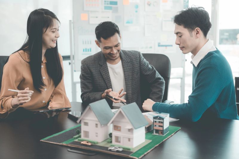 Business team signing investment agreement for residential real estate. Group of professionals in suits meeting in office with financial agreement documents on table.
