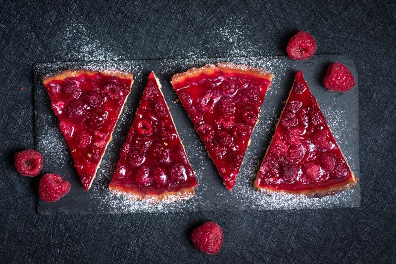 Delicious slices of raspberry tart topped with fresh ripe raspberries, beautifully arranged on a dark black background. Captured from a top-down perspective, ideal for bakery, dessert, and gourmet food photography themes.