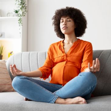 Pregnant woman meditating on sofa.