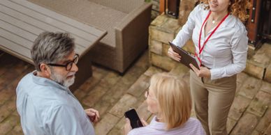 A couple talking to a smiling woman with a clipboard outdoors.
