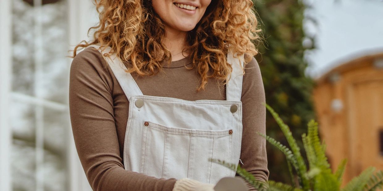 Woman smiling while gardening outdoors with gloves and overalls.