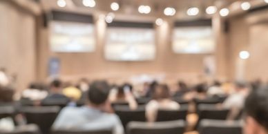 Blurry image of a conference or lecture hall with people seated.