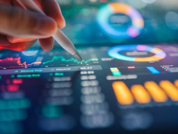 Hand using stylus on a digital financial dashboard with charts and graphs.