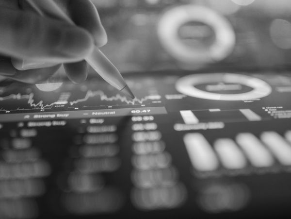Hand uses stylus to interact with colorful financial charts on a digital screen.