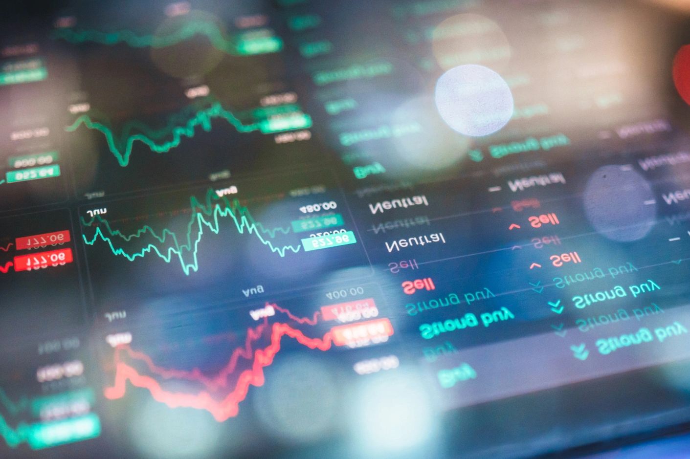 Blurred stock market graphs and data on a digital screen with green and red lines.