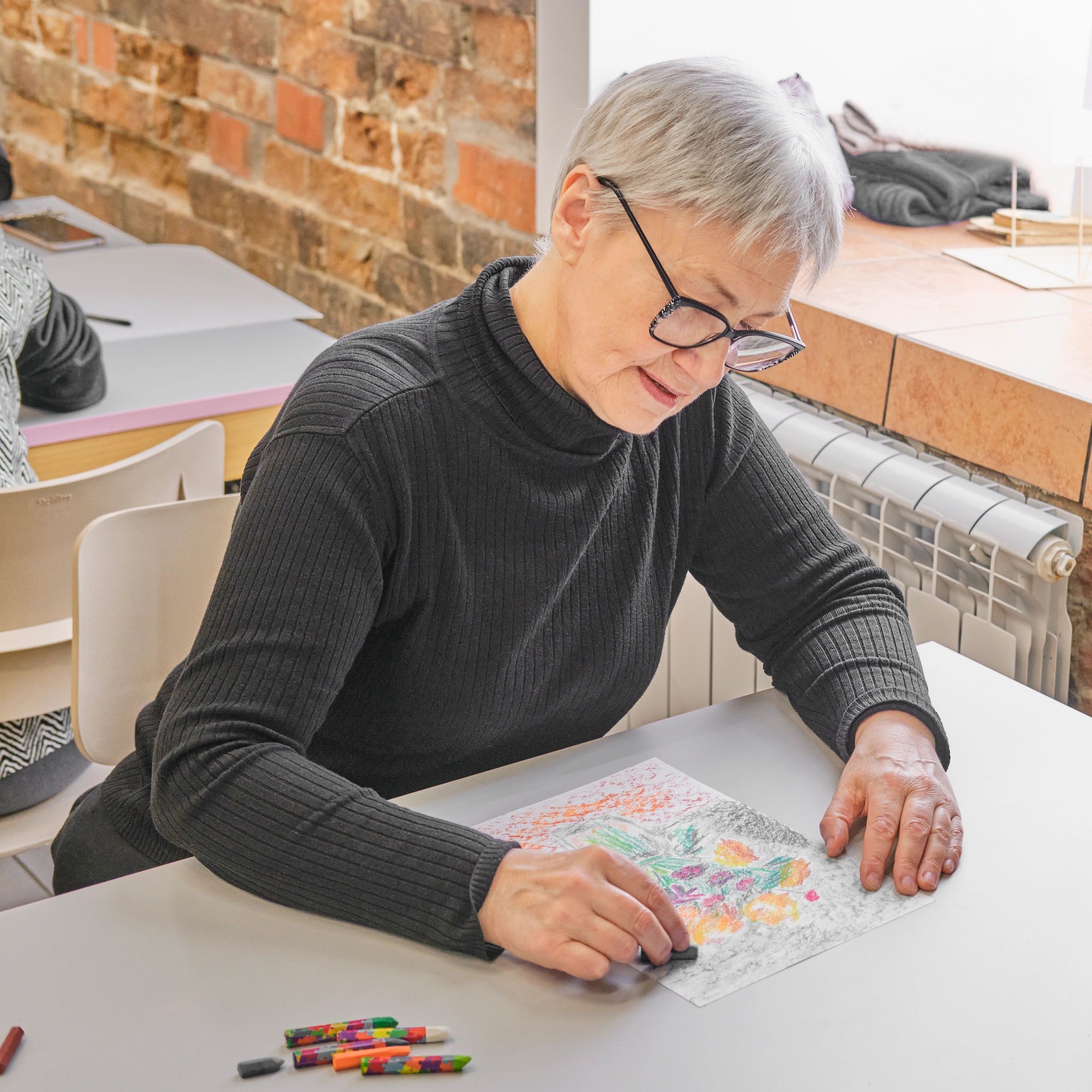 Elderly woman drawing with crayons at a table.