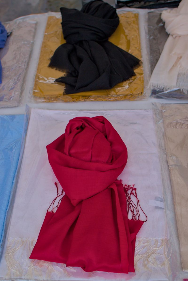 Brightly colored scarves are neatly arranged on display. A vivid red scarf lies centered over a soft white cloth. Textures and folds create a cozy and elegant feeling in the arrangement.