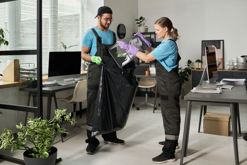 Cleaning workers throwing garbage in trash bag during cleaning in office