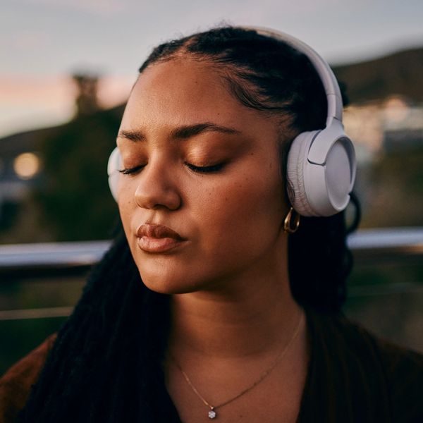 Woman with closed eyes enjoying music on white headphones outdoors.