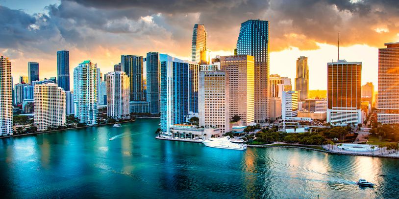 A vibrant city skyline at sunset with waterfront and boats.