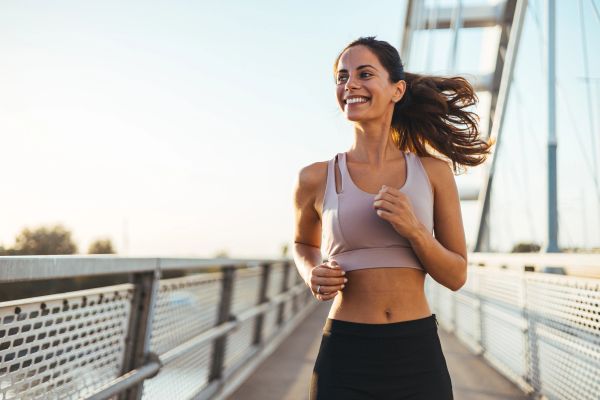 Smiling woman jogging on a bridge during sunrise.