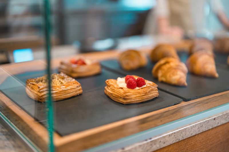 Close-up view of elegant pastry display featuring golden-brown croissants and delicate heart-shaped pastries topped with fresh raspberries, arranged on dark stone serving board.
