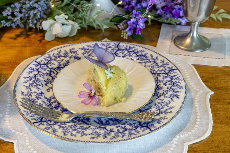 Lavender and lemon bundt cake with sugar wafer butterflies and borage flowers for garnish on a purple formal table setting.