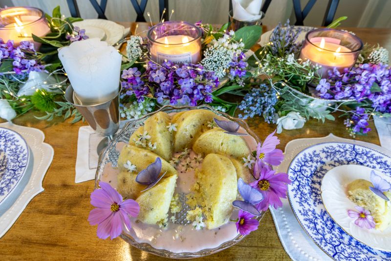 Lavender and lemon bundt cake with sugar wafer butterflies and borage flowers for garnish on a purple formal table setting.