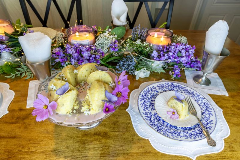 Lavender and lemon bundt cake with sugar wafer butterflies and borage flowers for garnish on a purple formal table setting.