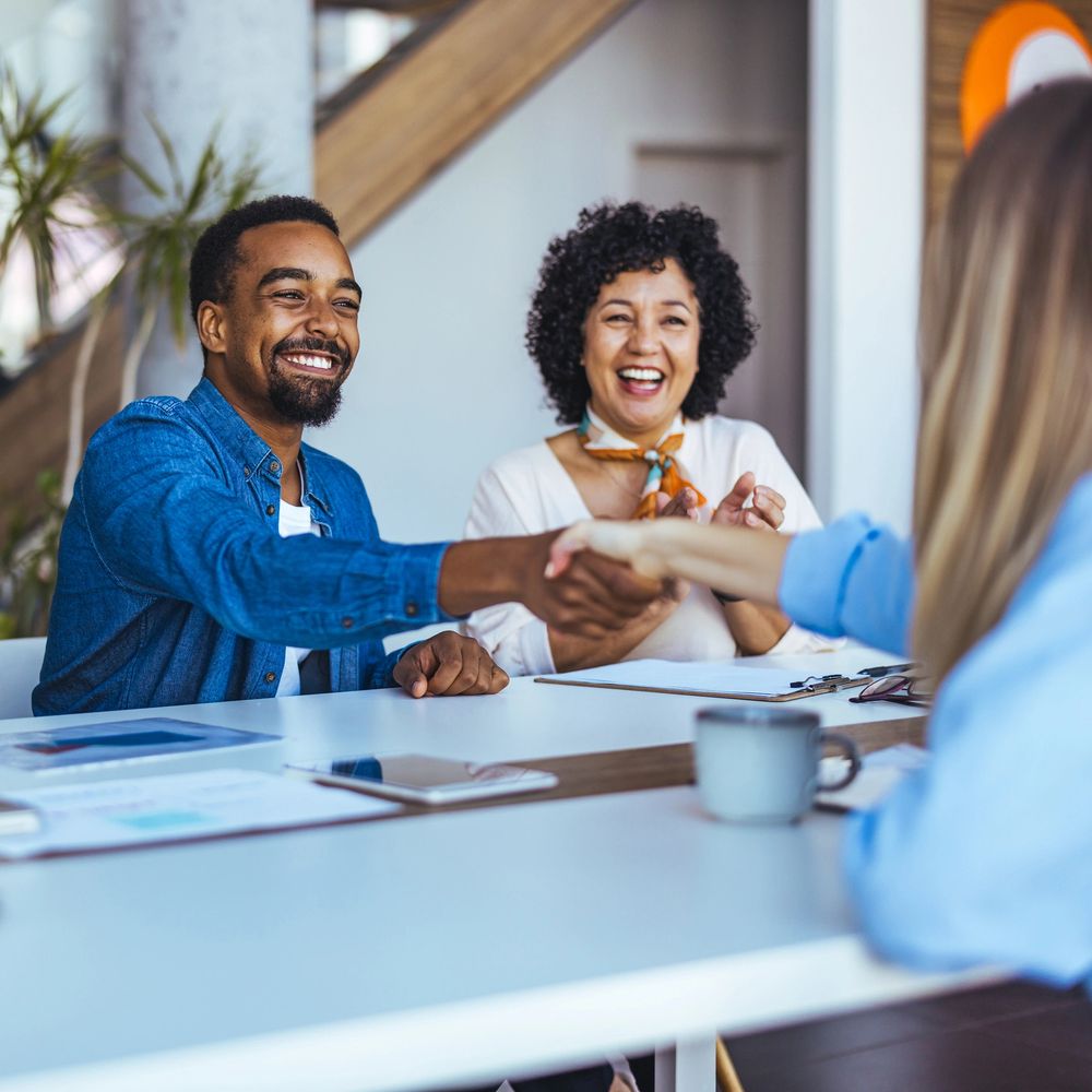 Two people happily shaking hands across a table during a meeting.