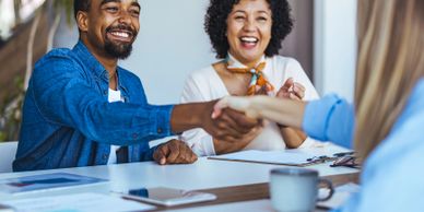 Two people happily shaking hands across a table in a meeting.