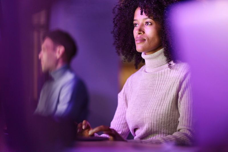 African American female graphic designer working on laptop while coding a language on desktop PC in the office.