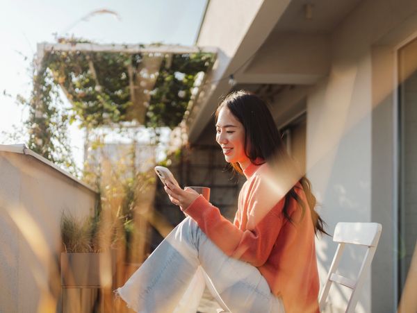 Woman in orange sweater using phone on balcony.