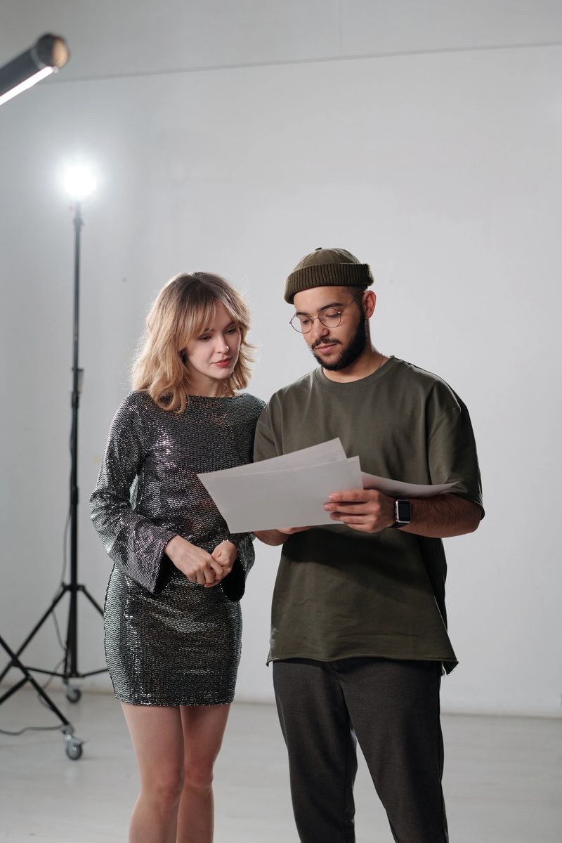 Vertical portrait of young actress consulting with assistant or director backstage and reading script notes in studio
