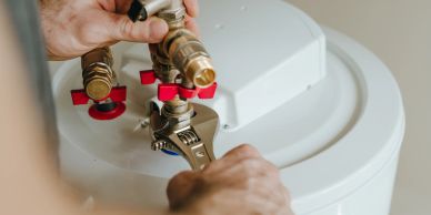 Person fixing a water heater valve with a wrench.